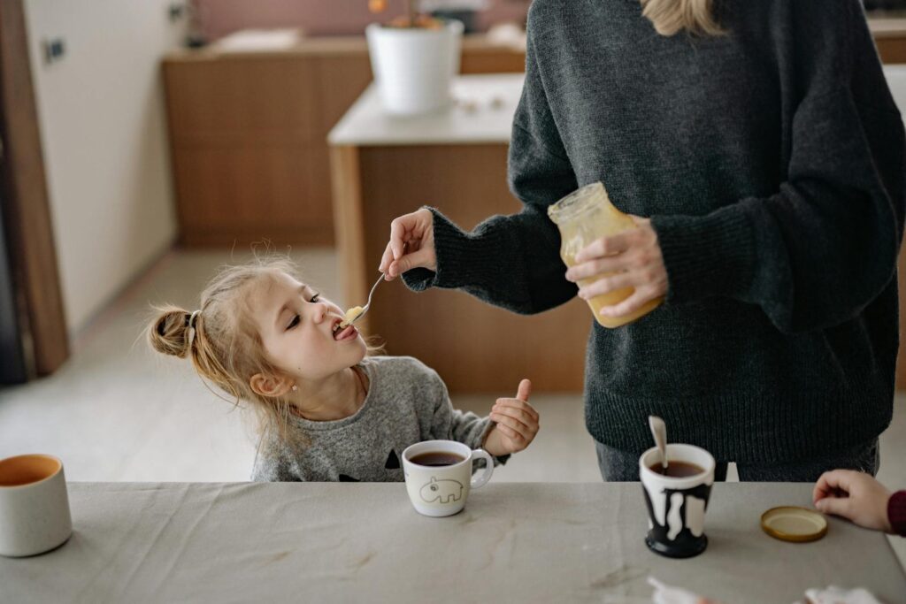 Woman Holding a Jar While Feeding a Girl with Honey