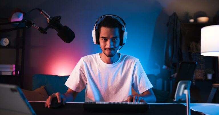 Young confident Asian man playing online computer video game, colorful lighting broadcast streaming live at home Gamer lifestyle, E Sport online gaming technology concept