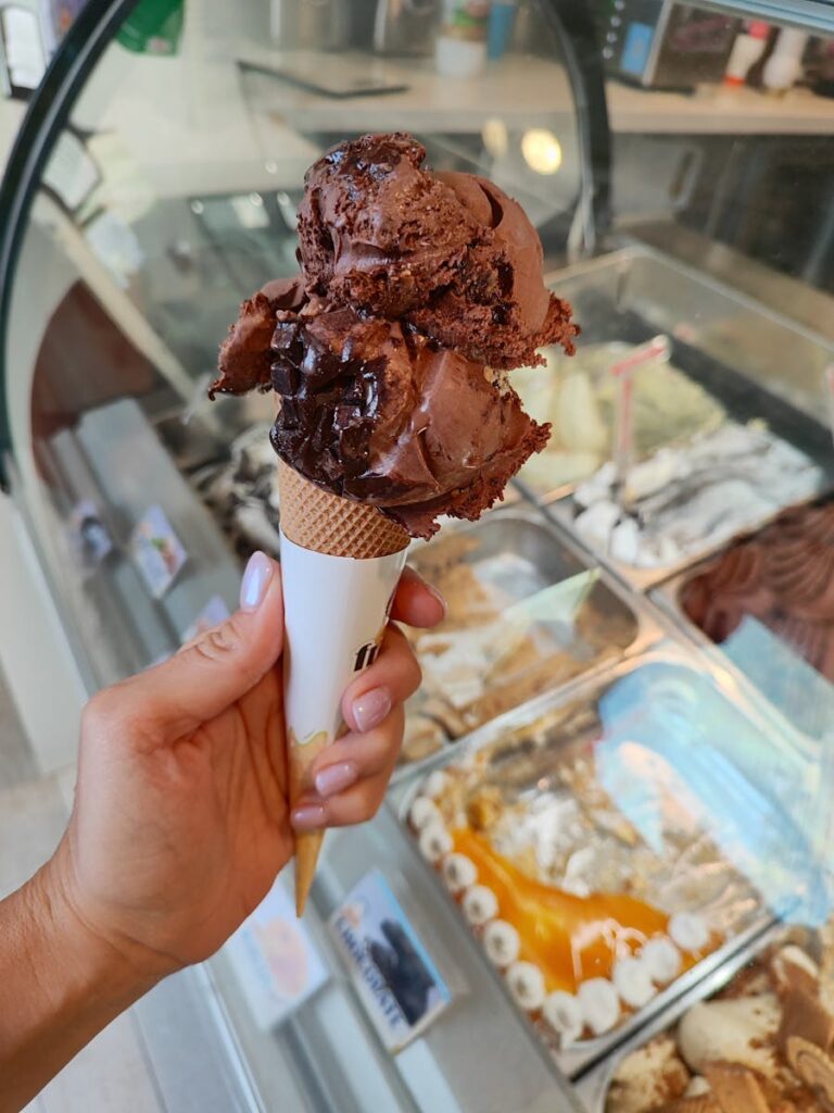 Close-up of a hand holding a chocolate ice cream cone in a vibrant gelateria.