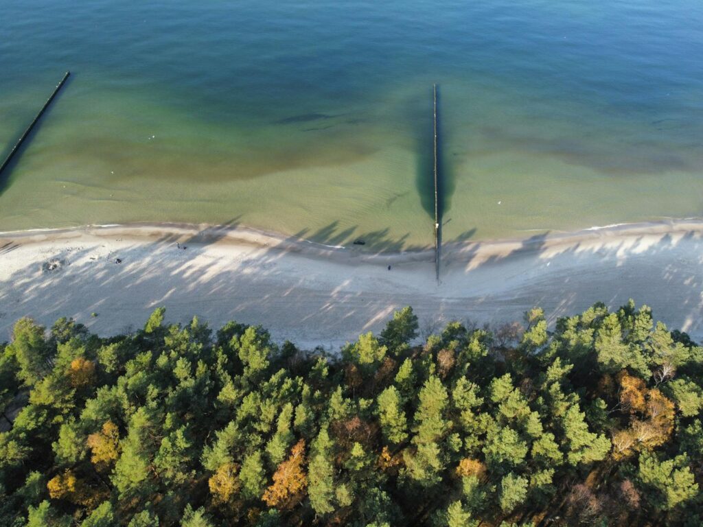 Stunning aerial image of Kołobrzeg beach with its emerald waters and lush greenery.