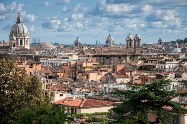 Panoramic view of the ancient rooftops and domes in Rome, Italy, showcasing historic architecture under a blue sky.