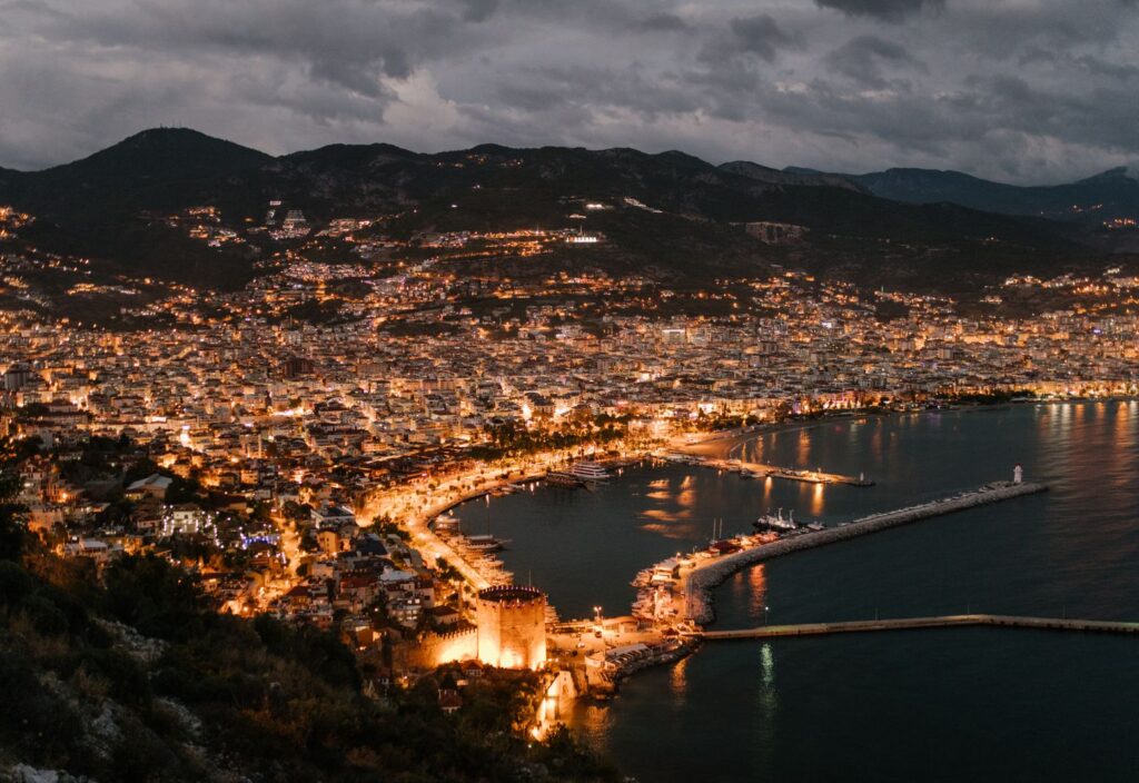 Amazing view of night coastal city located in highlands near calm sea and illuminated by bright electric lights